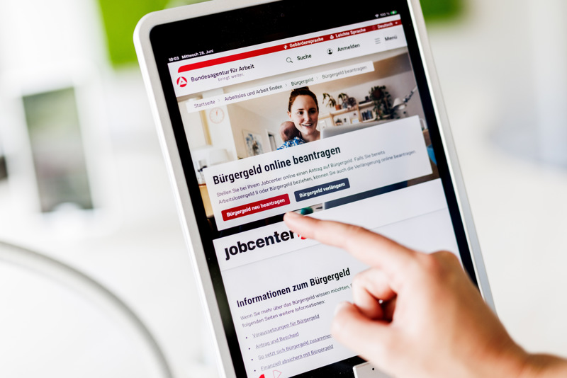 Eine Frau tippt auf einem Tablet auf einen Link zum Beantragen des Bürgergeldes im Kundenbereich im Jobcenter Berlin Mitte.