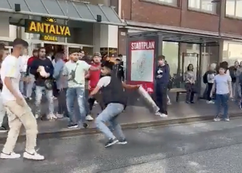 Mit einem Mülleimer bewaffnet, schlägt der Mann mit Weste auf einen weiteren ein.