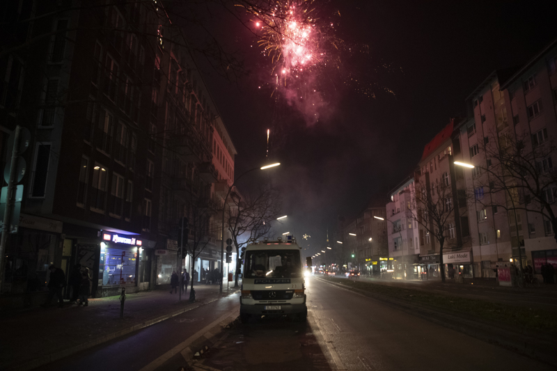 Ein Polizeiwagen parkt an Silvester am Straßenrand, während Feuerwerk in der Luft explodiert.