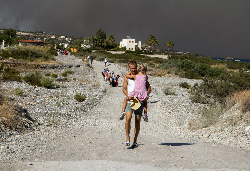 Ein Mann trägt ein Kind, als sie ein Gebiet verlassen, in dem ein Waldbrand auf der griechischen Insel Rhodos wütet.
