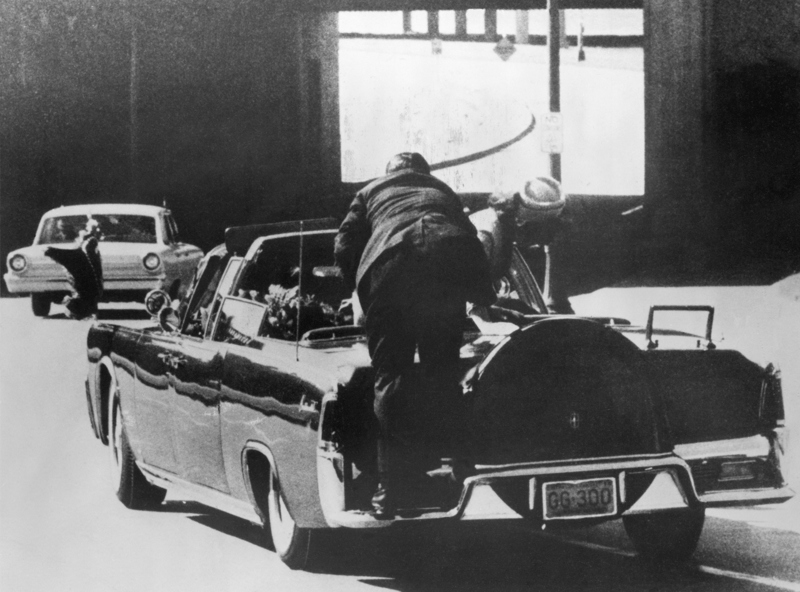 Leibwächter Clint Hill versucht verzweifelt, von hinten auf die Limousine von Präsident John F. Kennedy zu klettern, um ihn zu schützen.