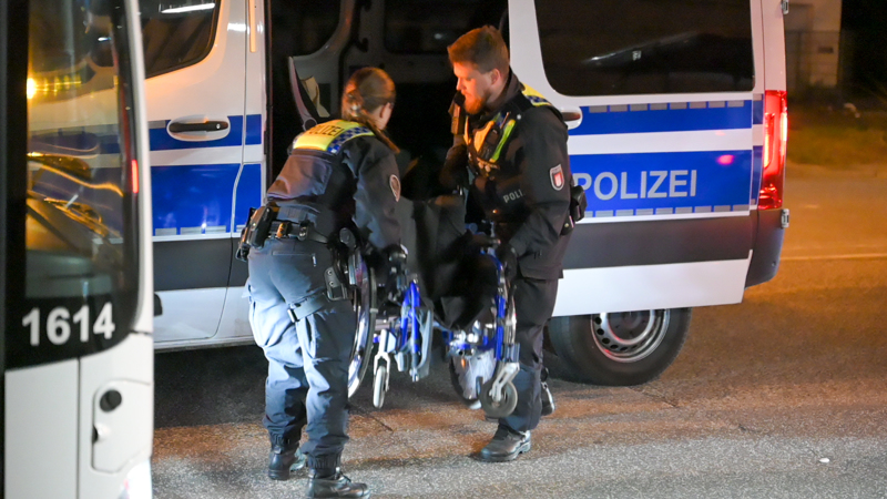 Beamte heben den Rollstuhl eines Opfers in ein Einsatzfahrzeug