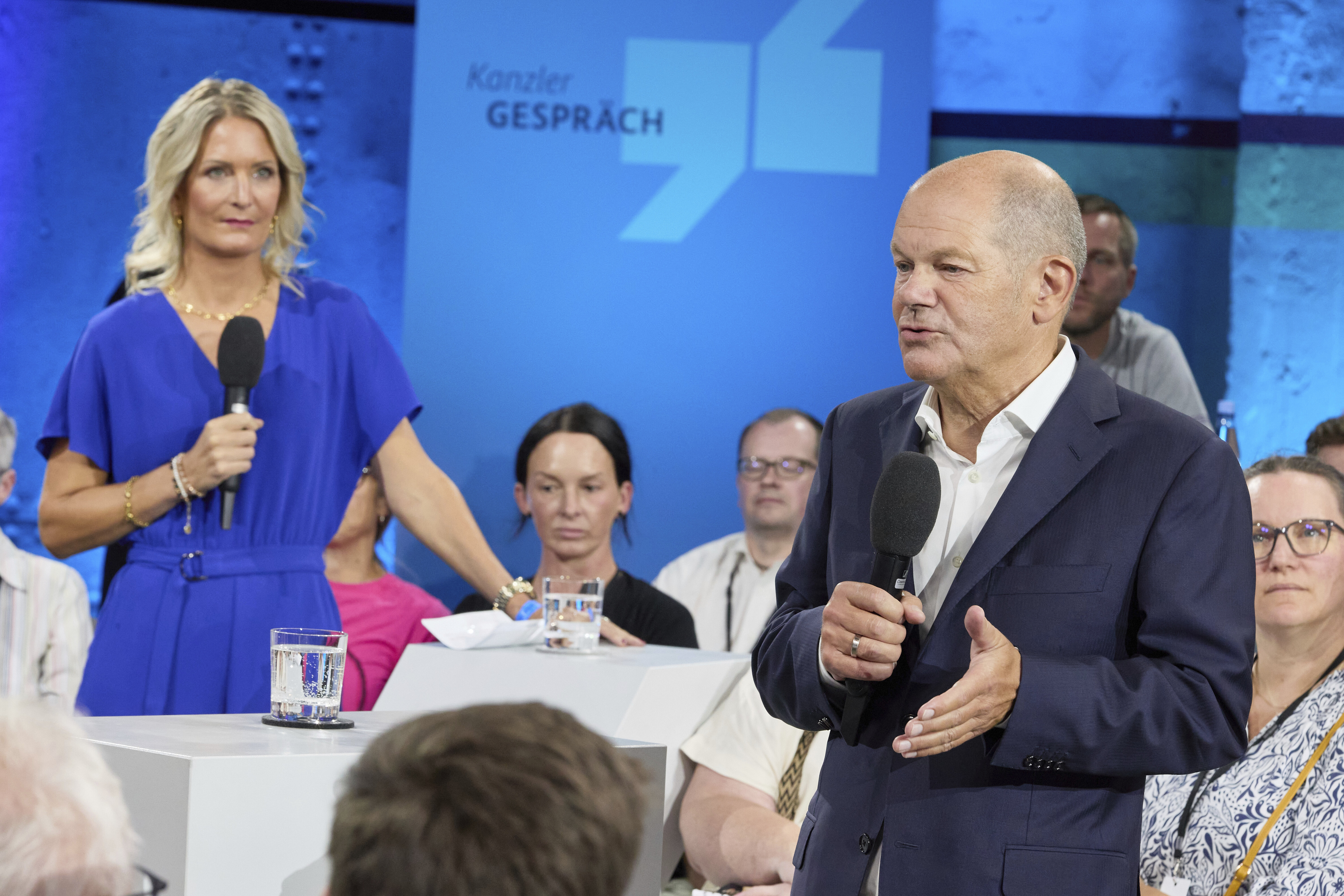 Olaf Scholz vor wenigen Wochen in Bremen – im Hintergrund die Journalistin Janna Betten, die von der Regierung Honorar kassiert.